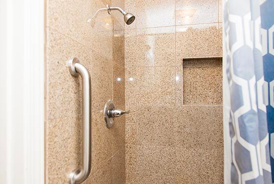 A tiled shower with a grab bar and a recessed niche.