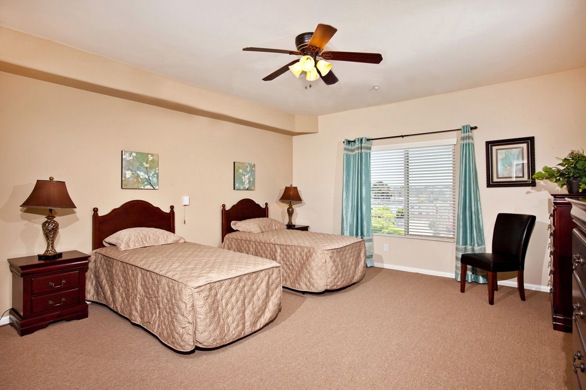 A spacious bedroom with two single beds, a ceiling fan, and a window with turquoise curtains.