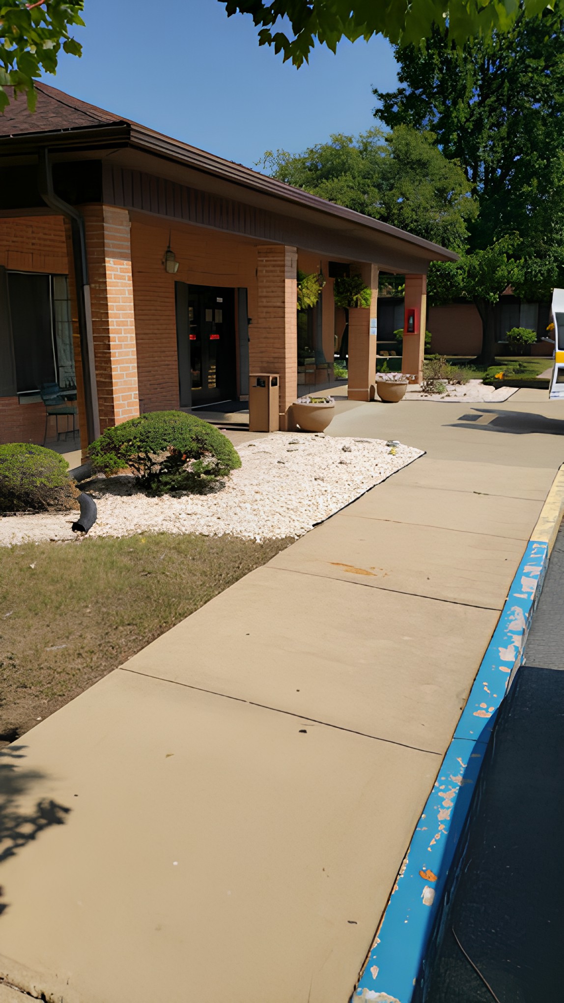 A brick building with a landscaped entrance area featuring bushes and a clean sidewalk.