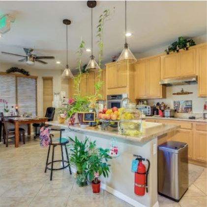 A modern kitchen with wooden cabinets, pendant lighting, and a central island adorned with plants and fruit baskets.
