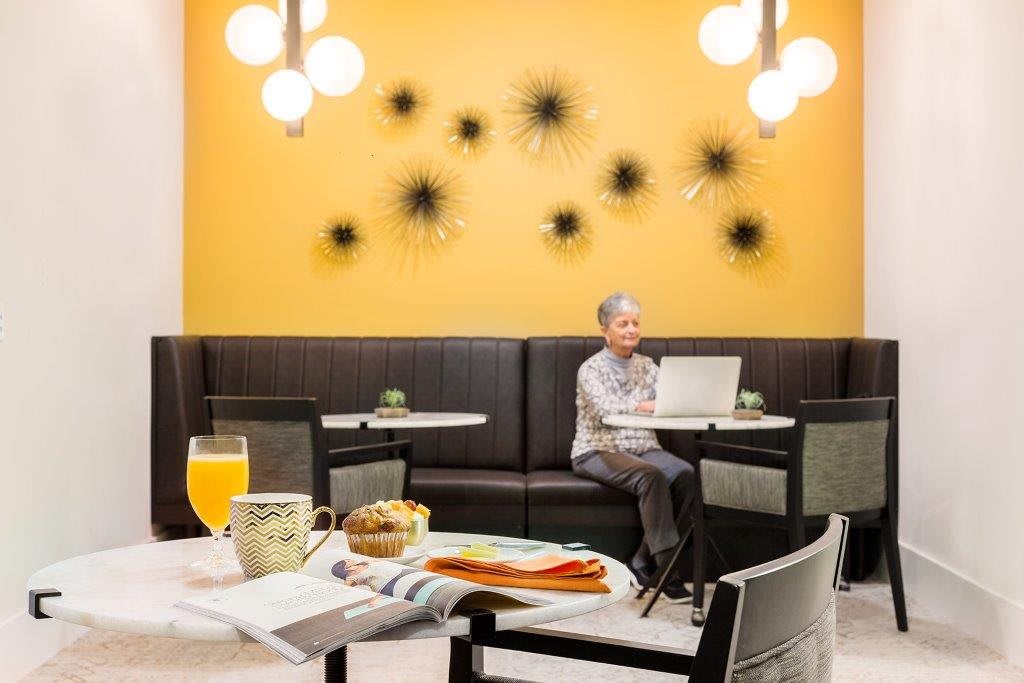 A person sitting in a modern cafe, working on a laptop with breakfast and orange juice on the table.