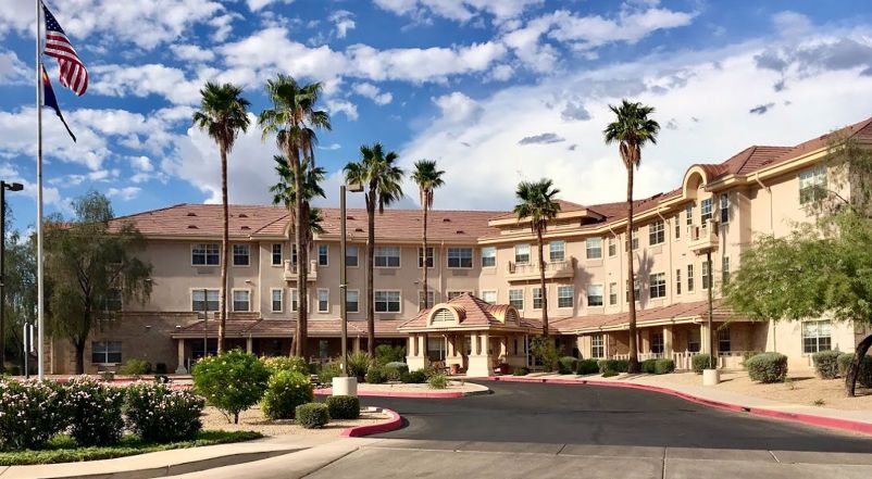 A large multi-story building surrounded by palm trees under a partly cloudy sky.
