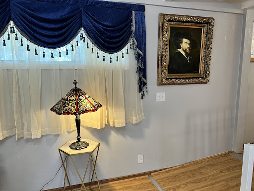 An elegantly styled corner of a room featuring a decorative lamp, rich blue curtains, and a classic painting.