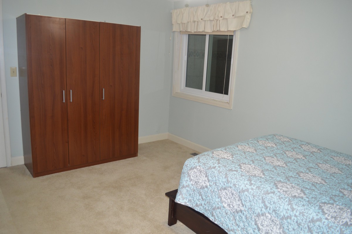 A simple bedroom with a wardrobe and a bed next to a window.