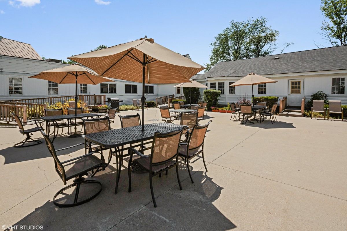A sunny patio with tables, chairs, and umbrellas in a residential setting.