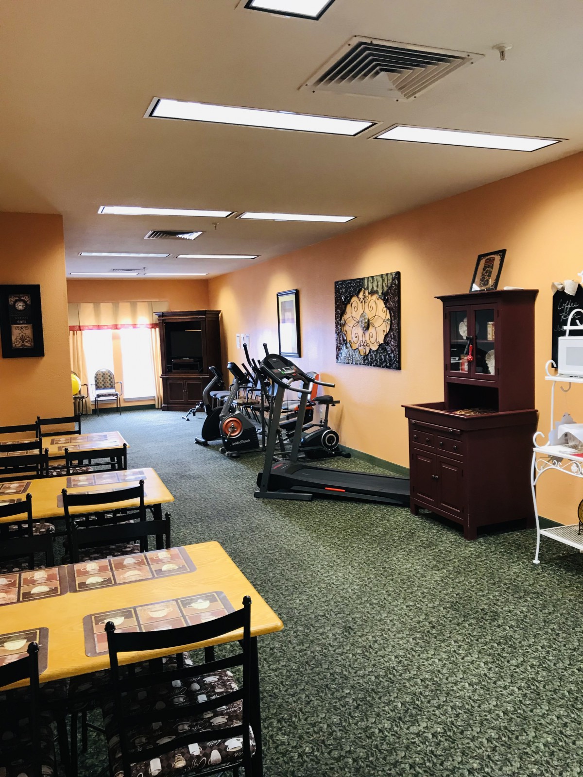 A multipurpose room featuring a dining area with tables and chairs, along with exercise equipment like treadmills.