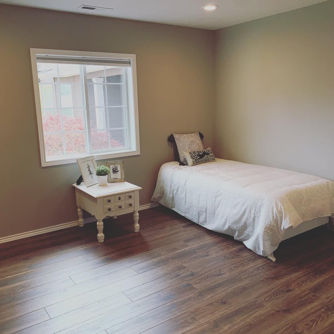 A minimalist bedroom with a single bed, side table, and wooden flooring.