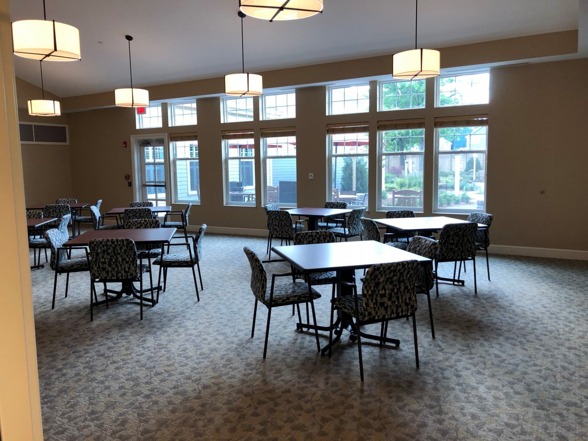 A spacious dining area with multiple tables and chairs, featuring large windows and overhead lighting.
