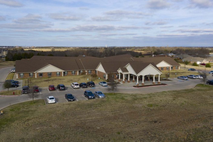Aerial view of a large building with a parking lot and cars under a cloudy sky.