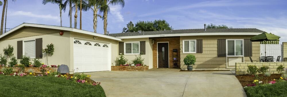 A suburban house with a garage and driveway, surrounded by plants.
