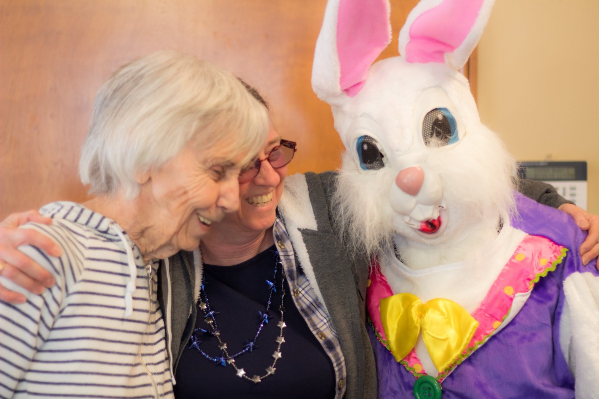 Two women smiling with a person in an Easter Bunny costume.