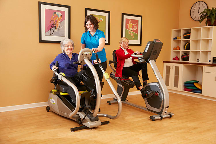 Seniors engaging in an indoor workout with fitness equipment, assisted by an instructor.