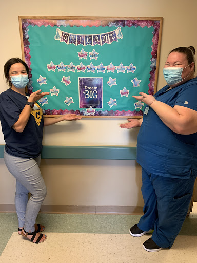 Two healthcare workers proudly showcasing a decorative bulletin board.