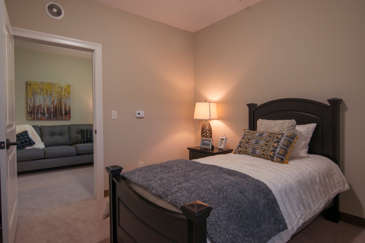 A cozy bedroom with a neatly made bed, lamp, and neutral decor.