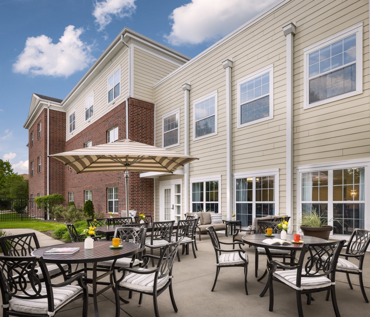 A cozy outdoor patio with tables, chairs, and umbrellas set against a modern residential building.