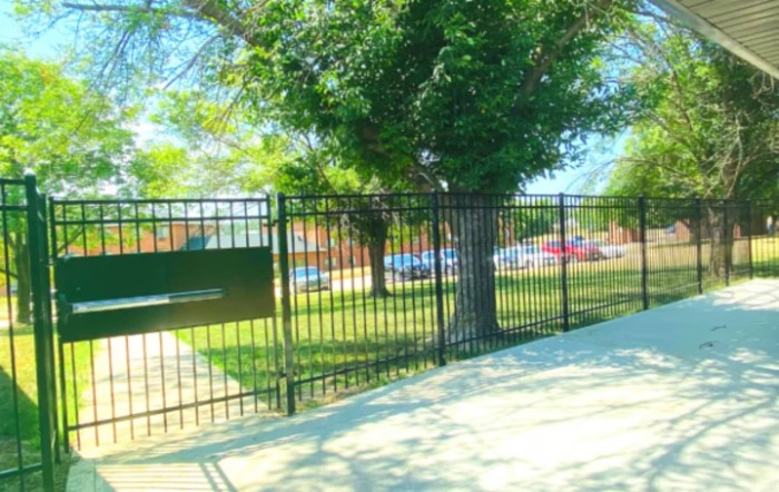A view of a fenced area with trees and a sidewalk on a sunny day.