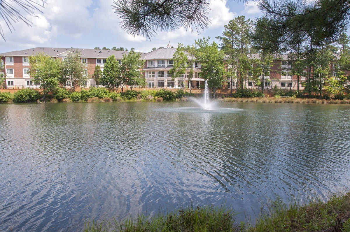 A serene pond with a fountain, surrounded by apartment buildings and lush greenery.