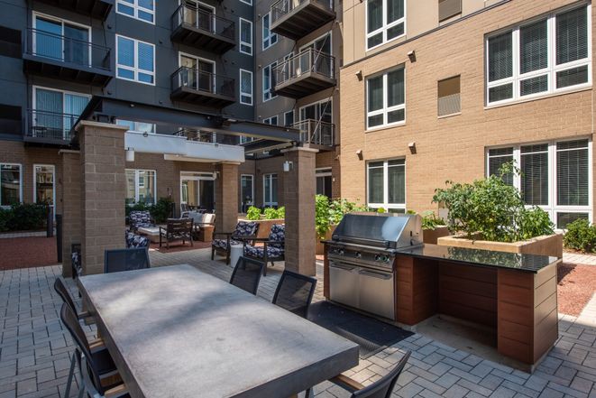 An outdoor patio area in an apartment complex featuring a dining table and grill.
