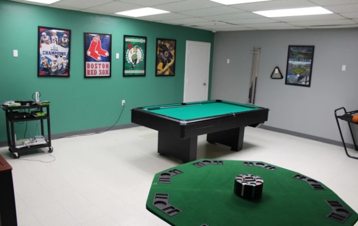 A game room featuring a pool table and poker table, decorated with sports posters on the walls.