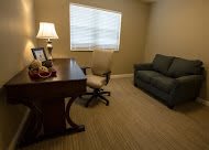 A small office space with a desk, chair, and sofa near a window.
