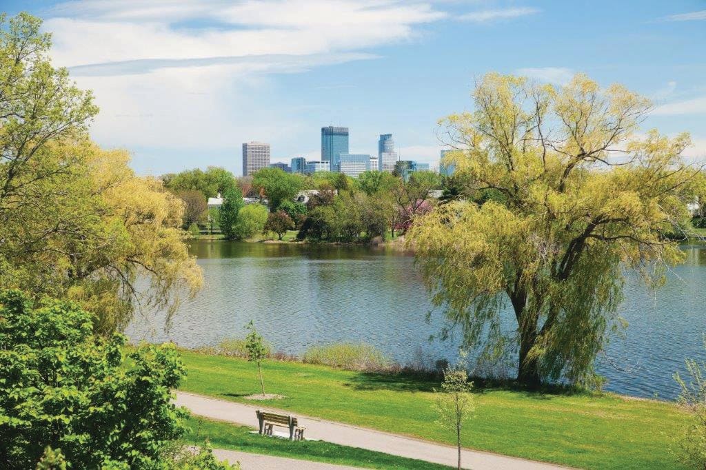 A peaceful park with a lake and an urban skyline in the background.