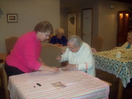 An elderly woman receives assistance at a table indoors.