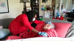 A healthcare worker in a mask and gloves takes care of an elderly person in bed.