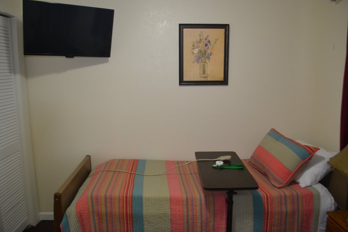 A small hospital room with a single bed, a wall-mounted television, and framed artwork.