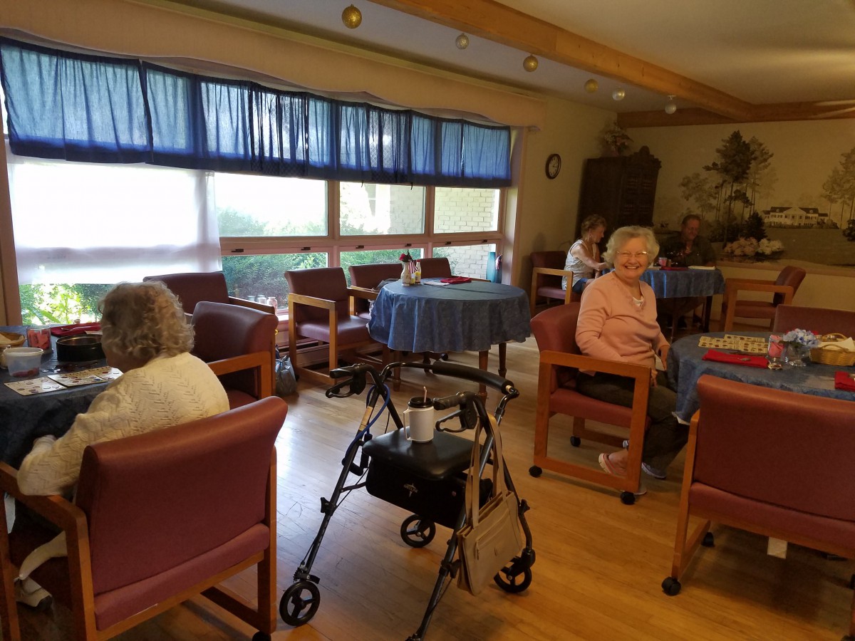 A cozy communal area in a nursing home with seniors seated and a walker nearby.