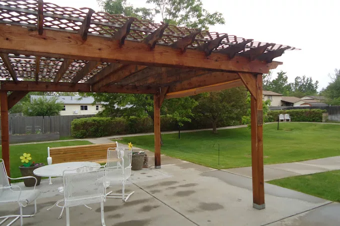 A wooden pergola stands over a patio area with outdoor furniture in a backyard setting.