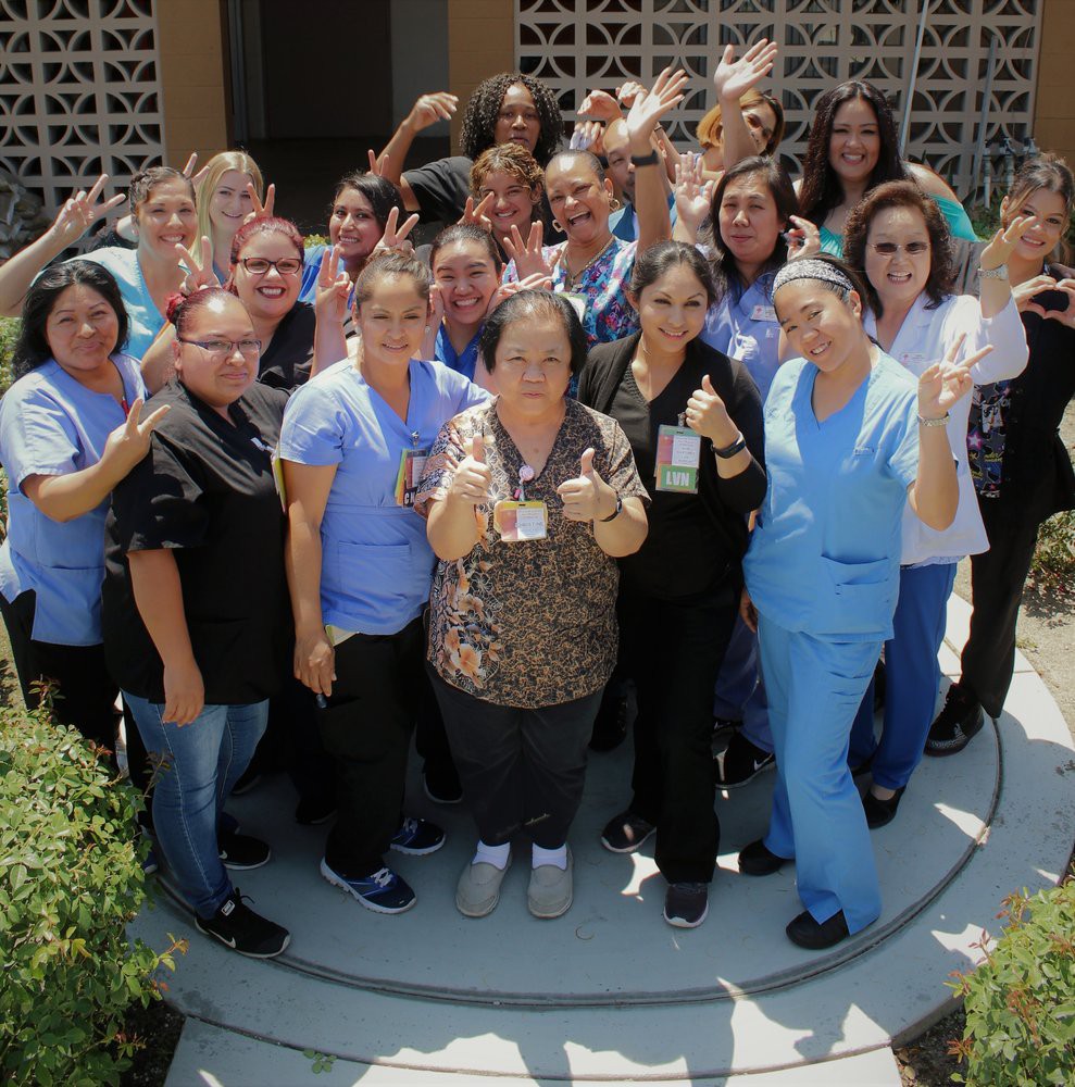 A group of healthcare workers smiling and posing for a team photo outdoors.