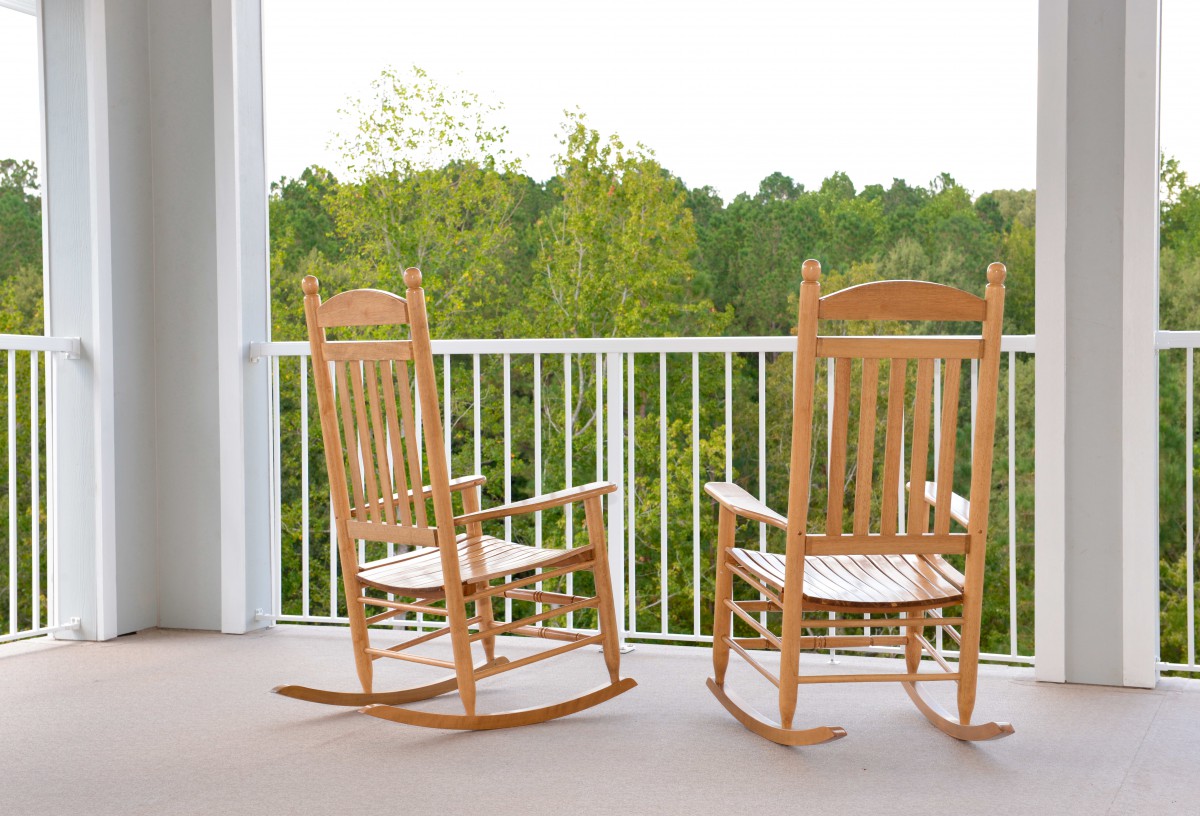 Two wooden rocking chairs on a balcony with a scenic view of trees in the background.
