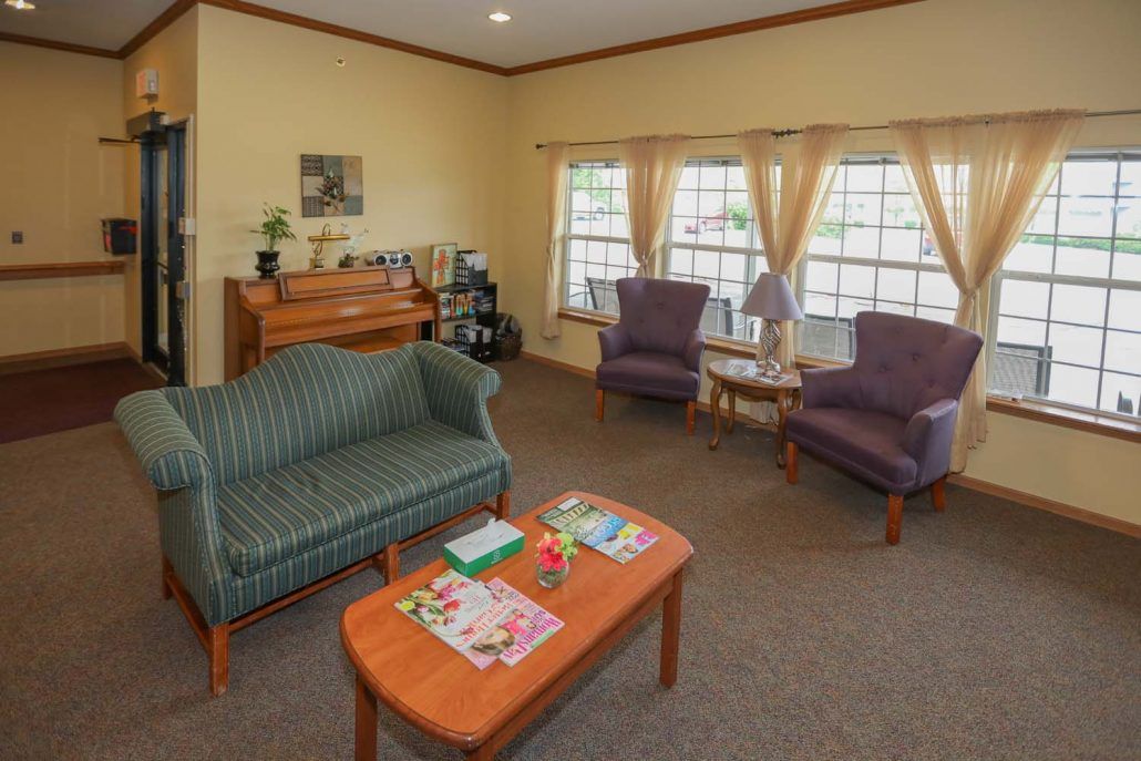 A cozy living room with a sofa, two armchairs, a coffee table, and a piano by the window.