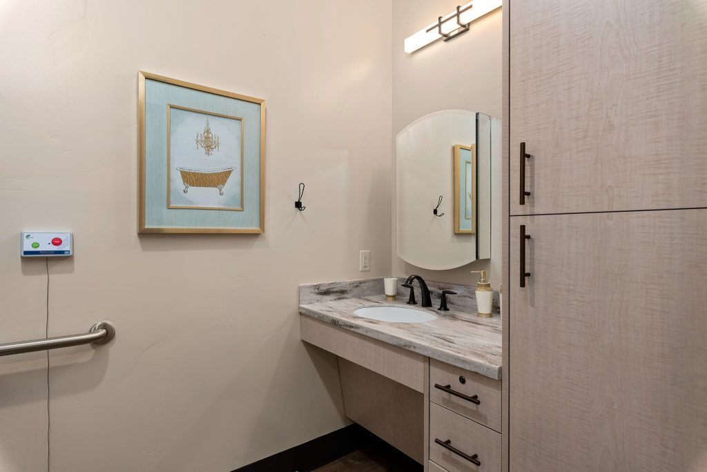 A small bathroom featuring a vanity with a marble countertop, an oval mirror, overhead lighting, and artwork on the wall.