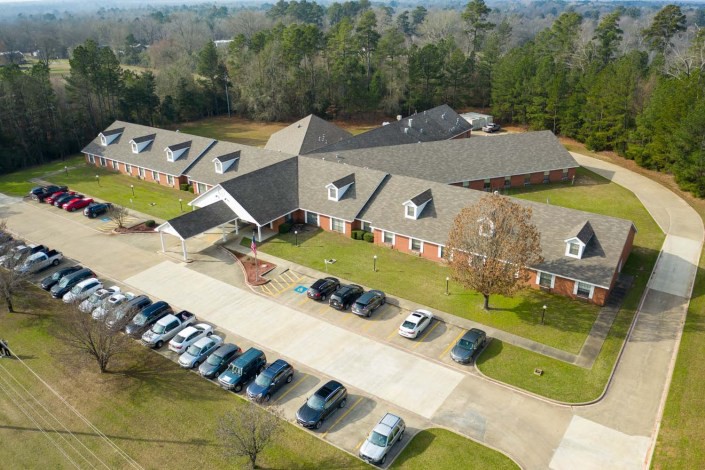 An aerial view of a residential building with an adjacent parking lot and surrounding greenery.