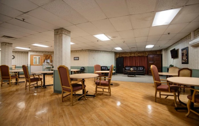 A well-lit community space with several tables and chairs arranged on a wooden floor.