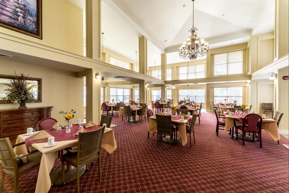 A spacious dining area with multiple tables and chairs, large windows, and a chandelier.
