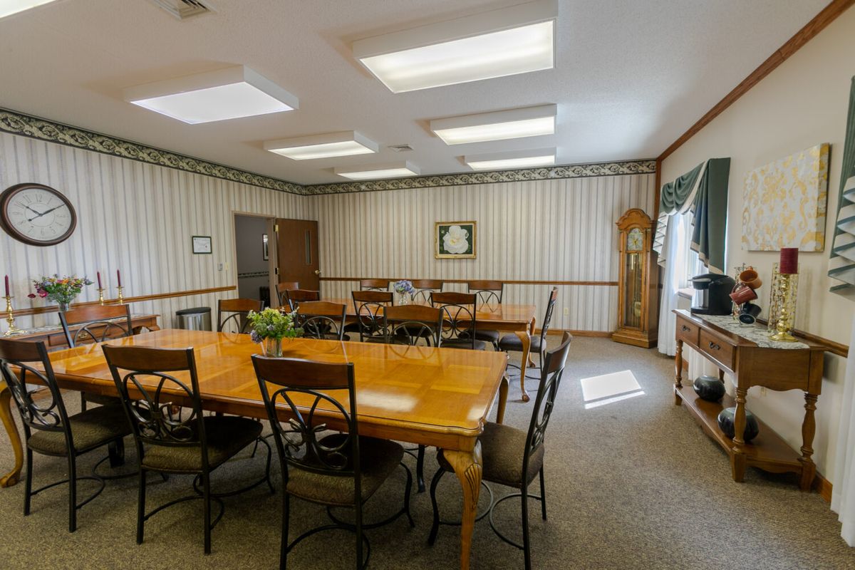 A conference room with a large wooden table surrounded by chairs, featuring a clock and decorative items.