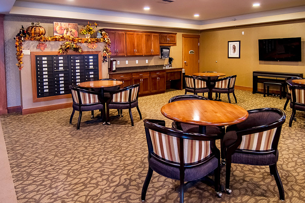 A cozy lounge area with round wooden tables and striped upholstered chairs, set on a carpeted floor under warm lighting.