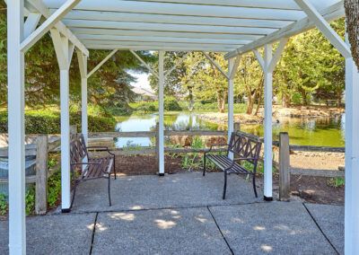 A peaceful gazebo with benches overlooking a serene pond in a park setting.