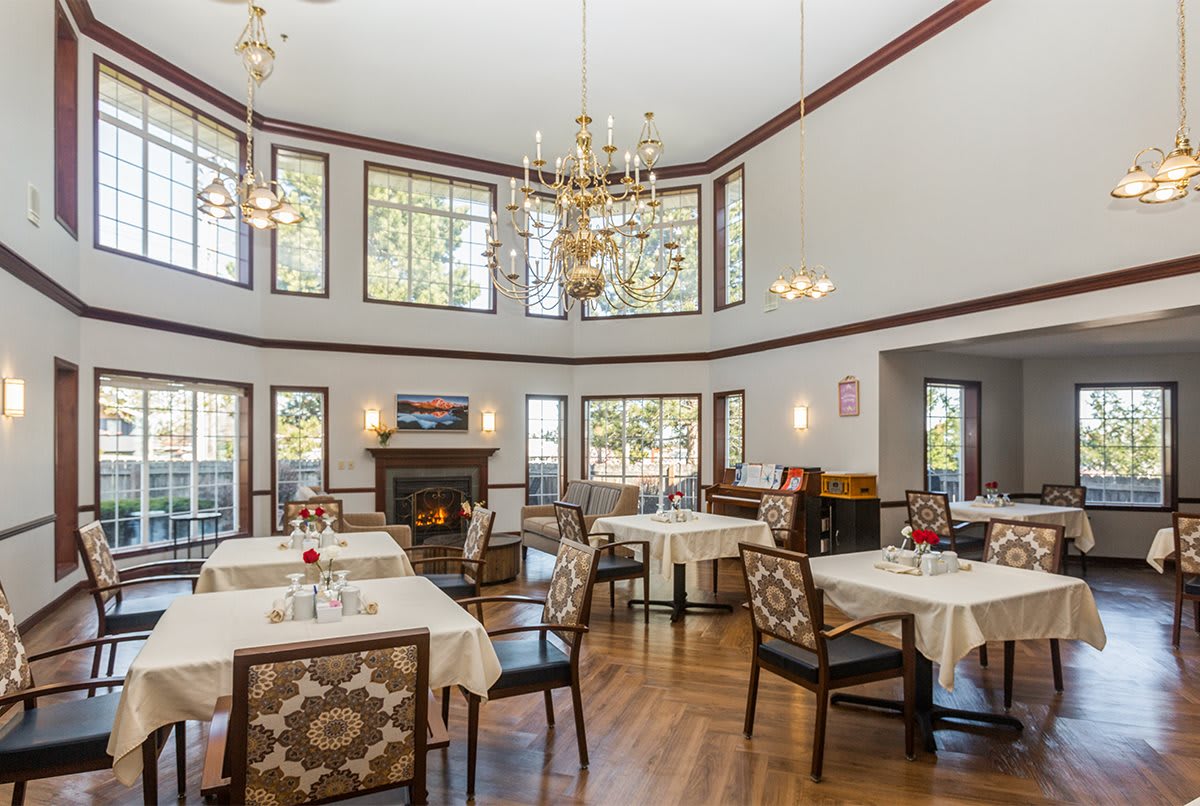 A spacious dining area with elegant chandeliers, large windows, and neatly arranged tables and chairs.