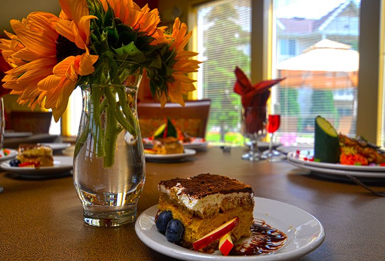 A slice of tiramisu on a plate with berries, set on a table adorned with sunflowers in a vase.
