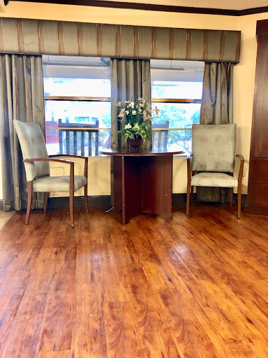 A cozy seating area featuring two chairs, a small table with plants, and large windows dressed with curtains.