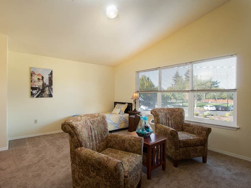 A cozy living room with two armchairs, a small table, and a large window allowing natural light in.