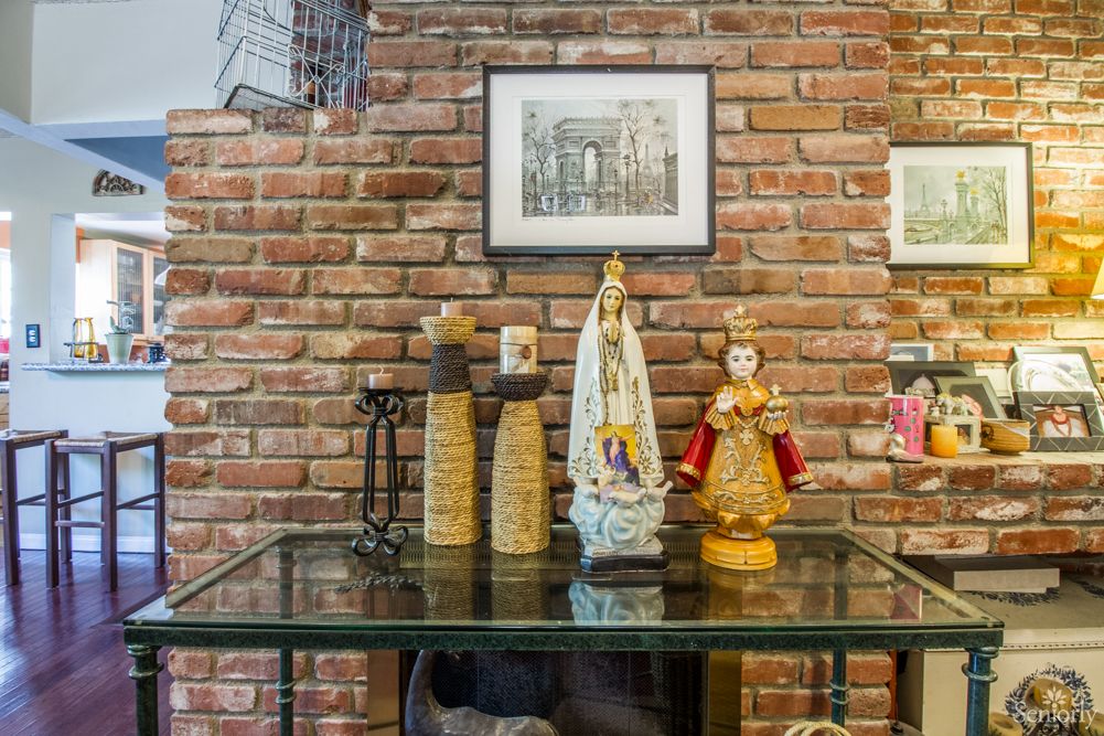 A glass table with decorative statues set against a brick wall adorned with framed artwork.