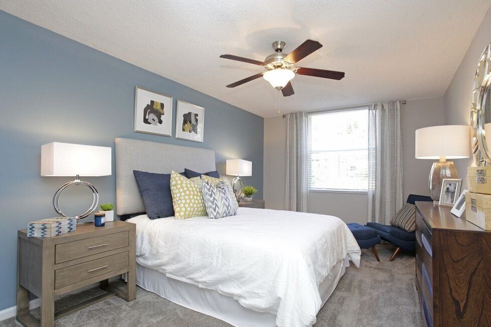 A cozy bedroom with a white bed, blue accent wall, and ceiling fan.