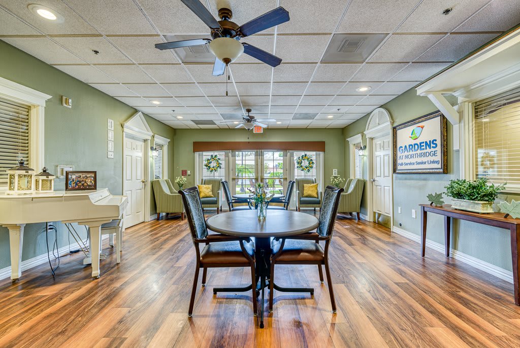 A cozy dining room with a central table and chairs, featuring large windows and wooden flooring.