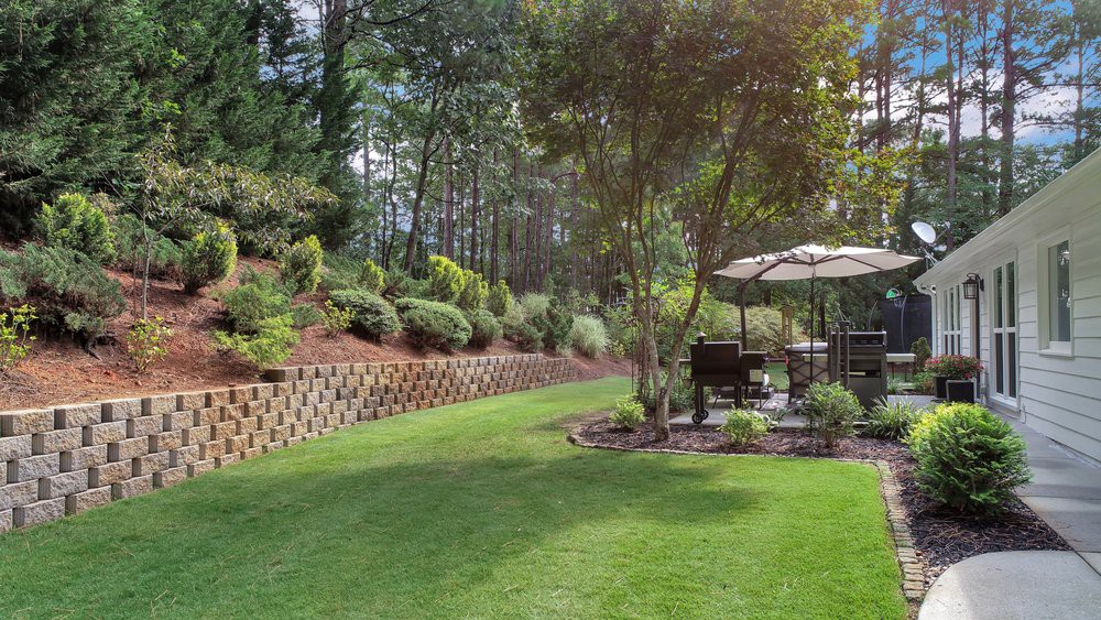 A beautifully landscaped backyard with a green lawn, trees, and patio furniture under an umbrella.