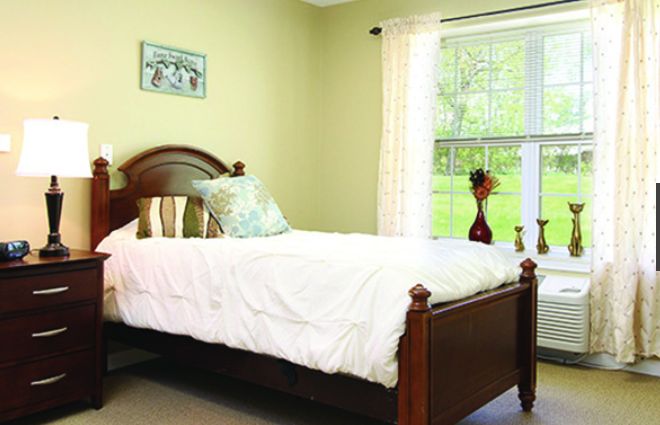 A cozy bedroom with a wooden bed and a large window letting in natural light.