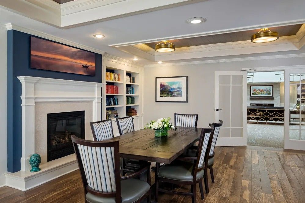 A modern dining room featuring a fireplace, bookshelves, and a hardwood floor.